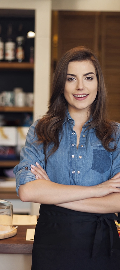 Mulher de pele clara, sorrindo. ela utiliza camisa social jeans, está com braços cruzados.